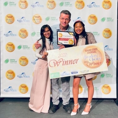 Three people stand smiling, holding a large 2022 Winner check and a framed certificate on a stage with a step-and-repeat Idaho State Journal Readers Choice Awards backdrop.