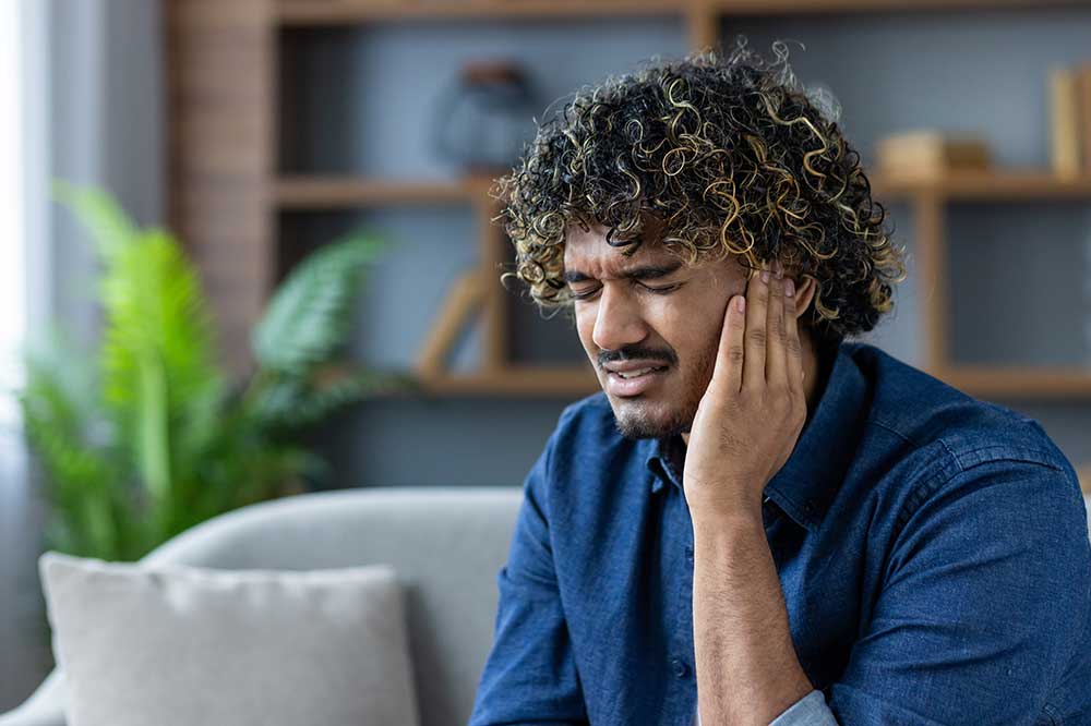 Man in a denim shirt holding his ear at home with a clogged ear feeling, from Centrum Hearing & Audiology in Pocatello, ID